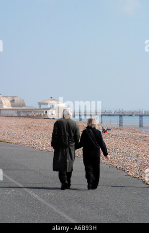 Ein Paar mittleren Alters, das Hand in Hand an der verlassenen Strandpromenade in Worthing, West Sussex, läuft. VEREINIGTES KÖNIGREICH. Stockfoto