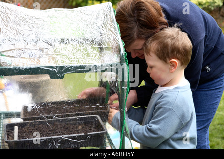 Mutter hilft ihrem kleinen Sohn in kleinen plastischen Gewächshaus für die Keimung im Frühjahr gepflanzten Samen Schalen platzieren Stockfoto