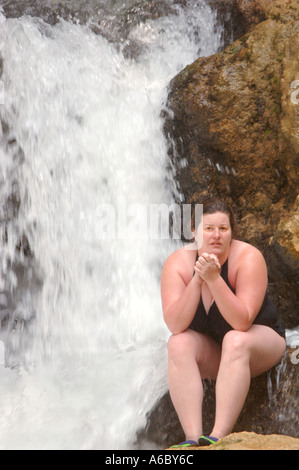 Vertikale Farbbild einer jungen Frau im Badeanzug sitzt auf einem Felsen vor einem Wasserfall Stockfoto