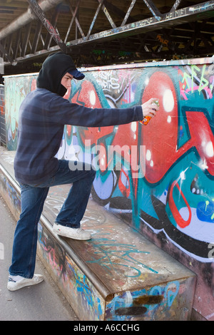 Ein mit Kapuze besprühter Jugendlicher sprüht Graffiti und markiert sein Etikett auf einem Skatepark in Southport Merseyside. Stockfoto