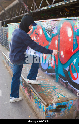 Ein mit Kapuze besprühter Jugendlicher sprüht Graffiti und markiert sein Etikett auf einem Skatepark in Southport Merseyside. Stockfoto