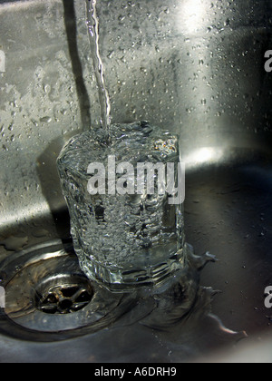 Glas in eine Edelstahl-Spüle mit Wasserhahn Wasser hinein laufen. Stockfoto