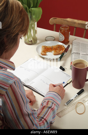 Weibchen mit ihrem Tagebuch auf Küchentisch Stockfoto
