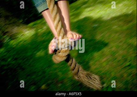 Die Füße eines zehnjährigen Mädchens mit rot lackierten Zehennägeln schwingen auf einem verknoteten Seil schwingen über dem grünen Rasen im Sommer Stockfoto