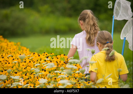 Die Rückseiten der beiden leger gekleidet Schwestern mit Schmetterling Netze gehen auf ein Tages-Abenteuer in einem Garten von Black-Eyed Susans. Stockfoto