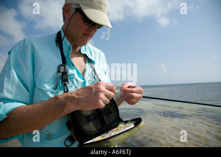 BELIZE Ambergris Caye erwachsenen männlichen Fliegenfischen in Wohnungen entlang der Küstenlinie für Bonefish Änderung fliegen Halt Rod unter Arm ziehen Sie Knoten Stockfoto
