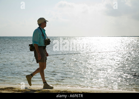 BELIZE Ambergris Caye Männchen gekleidet für Fliegenfischen Spaziergang Strand und Küste tragen Stab waten Stiefel silhouette Stockfoto