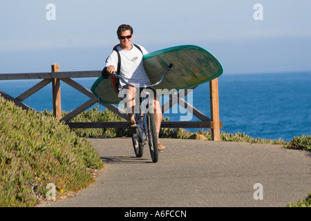 Ein Mann, mit dem Fahrrad mit einem Surfbrett über dem Ozean in Santa Cruz, Kalifornien Stockfoto