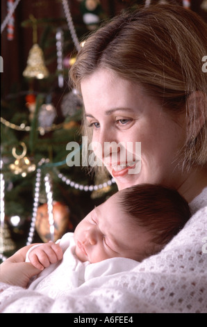 Christmas baby vierundzwanzig Jahre alt happy fröhlich lächelnd Ausdruck der Mutter & 5 Woche alt neu geboren Schlafen baby boy neben Xmas Tree England Großbritannien Stockfoto