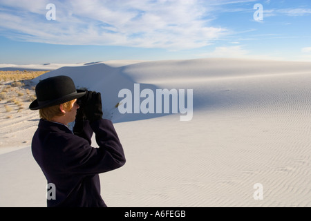Mann mit Mantel und Bowler Hut Blick durch ein Fernglas auf weiße Sanddüne Wüste Stockfoto