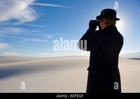 Mann mit Mantel und Bowler Hut Blick durch ein Fernglas auf weiße Sanddüne Wüste Stockfoto