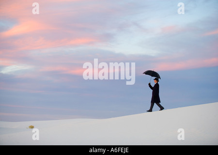Mann mit Mantel und Holding-Dach in Sanddünen Wandern Stockfoto
