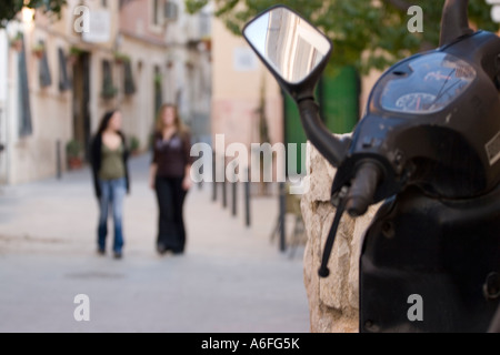 Zwei junge Frauen zu Fuß entlang spanische Straße mit Mo-ped im Vordergrund. Stockfoto