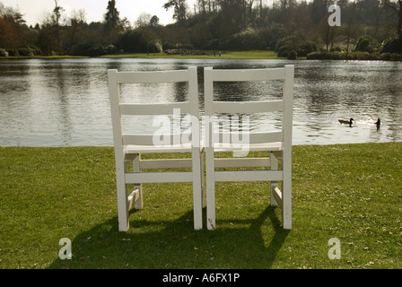 zwei weiße Holzstühle auf einer Wiese mit Blick auf einen See Stockfoto