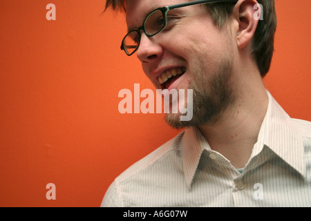 Junge blonde Mann mit Kunststoff-Gläser rahmt lächelt stehend gegen eine orange Wand Stockfoto