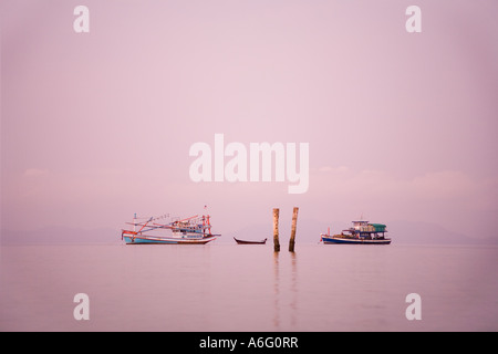 Zwei traditionelle Boote offshore; Thai Fischerbooten in der Morgendämmerung Sonnenaufgang, wie die Sonne über dem ruhigen Andaman Meer, Krabi Beach Resort, Thailand Stockfoto