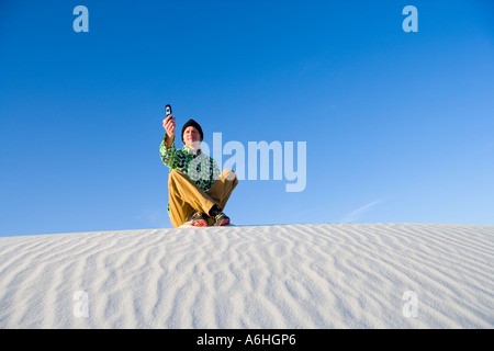 junger Mann sitzt auf der Sanddüne mit Bild-Telefon Stockfoto