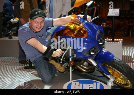 Mann auf statische Motorrad Messe vorgibt, das Fahrrad zu lehnen. Stockfoto