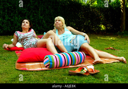 Junge Frauen auf Kissen in einem Garten liegen Stockfoto