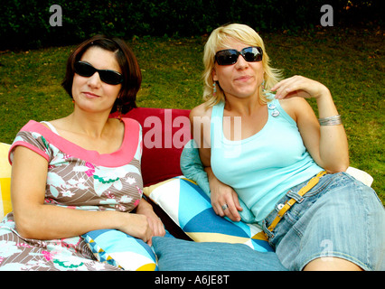 Zwei junge Frauen in Sonnenbrille liegend auf Kissen in einem Garten Stockfoto