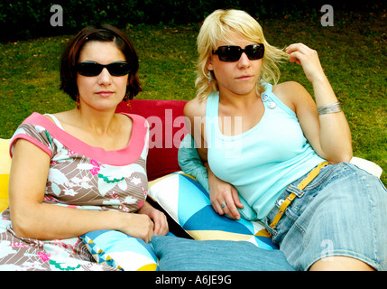 Zwei junge Frauen in Sonnenbrille liegend auf Kissen in einem Garten Stockfoto