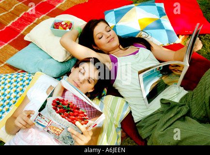 Junge Frauen in einem Garten auf Kissen liegend und Magazine lesen Stockfoto