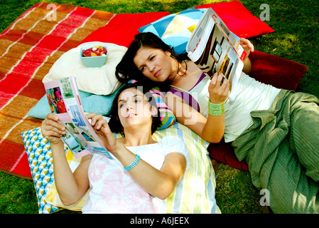 Junge Frauen in einem Garten auf Kissen liegend und Magazine lesen Stockfoto