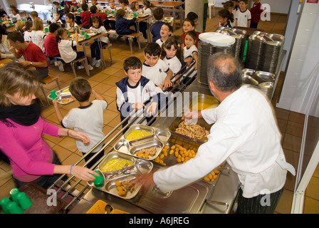 Schule MAHLZEITEN MITTAGESSEN KANTINE SERVICE ABENDESSEN GESUND service Junior und Kleinkinder Schulkinder in geschäftigen Schulkantine mit Küchenchef und Lehrer Aufsicht Stockfoto