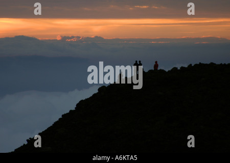 Silhouetten der vier Leute beobachten Sonnenaufgang von über den Wolken am Haleakala Krater in Maui, Hawaii Stockfoto