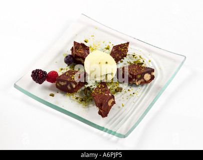 SCHOKOLADEN-BROWNIE-STÜCKE MIT OBST, EIS UND PISTAZIEN GARNIEREN Stockfoto