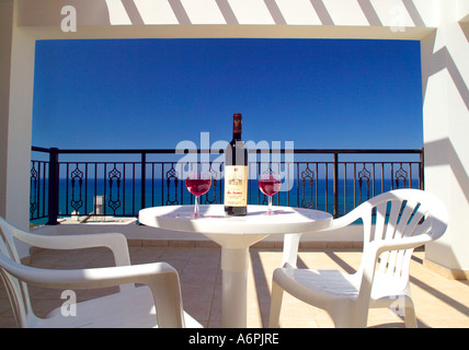 EINE TISCHDEKORATION MIT ROTWEIN AUF EINEM SONNIGEN BALKON MIT BLICK ÜBER BLAUEN HIMMEL UND DAS MEER IN ZYPERN Stockfoto