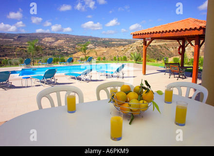 ORANGENSAFT UND ZITRUSFRÜCHTE AUF HOLZTISCH MIT POOL UND DIE BERGE IM HINTERGRUND IN ZYPERN Stockfoto