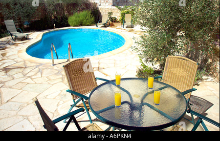 TABELLE MIT ORANGENSAFT ALFRESCO IN DER ABENDSONNE MIT POOL IM HINTERGRUND Stockfoto