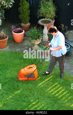 Blick hinunter auf den Hausgarten mit 63 Jahre alte Frauen mit elektrischen Hover Mäher Rasen schneiden Stockfoto