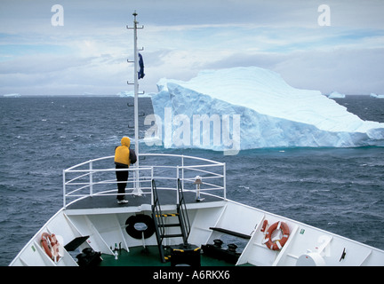 ein Passagier in Gelb steht auf dem Bug eines Kreuzfahrtschiffes gekleidet, wie es nähert sich ein einsamer Eisberg auf der Weddell-See-antarcitic Stockfoto