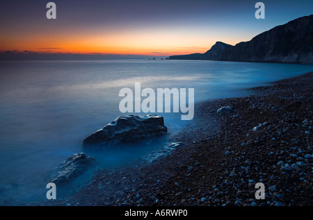 Das Nachleuchten nach Sonnenuntergang leuchtet den Himmel in der Worbarrow Bay in Dorset.  Das Wasser ist vollkommen ruhig Stockfoto