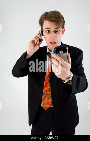 BUSINESS-MANN IM DUNKLEN ANZUG SUCHEN GESTRESST AUF TELEFONIEREN MIT HANDY UND HALTEN PERSÖNLICHER ORGANIZER POCKETPC Stockfoto