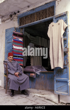 Afrika, Marokko, Chefchaouen (aka Chaouen), Ladenbesitzer in traditionelle Djellaba (Robe mit Kapuze) und Fez mit Decke hinter (MR) Stockfoto