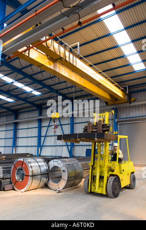 Ladung heben Fahrzeug im Warehouse, industriellen Umfeld. Fahrer hält das Lenkrad, Metallplatten, die in die Luft gehoben Stockfoto