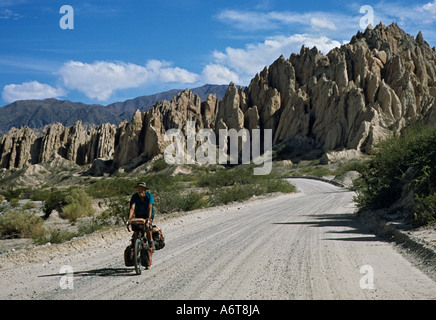 Einsame männliche Radfahrer auf grobe Ripio sandige Straße mit seltsamen Felsformationen im Hintergrund im nördlichen Argentinien Stockfoto