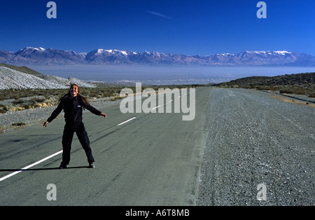 Weibliche Radfahrer gekleidet in schwarz auf leere Straße in weiten Argentinien Landschaft mit Palette von Anden Berge und blauer Himmel Stockfoto