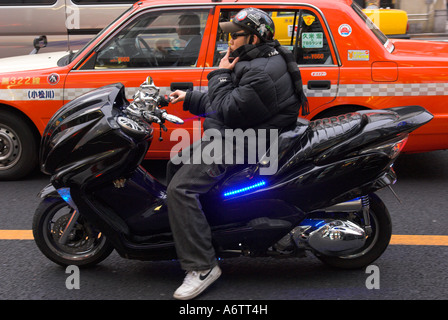 Tokyo Japan Honshu Scooter junger Mann schwarz tragen und Gerüschtes, einer stilvollen schwarzen Motorroller mit Blaulicht und Taxi in bkgd Stockfoto