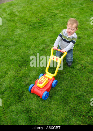 Kleiner Junge Mähen des Rasens mit Kunststoff-Spielzeug Rasenmäher Stockfoto