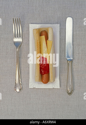 Hot-Dog-Wurst mit Käse in Brötchen auf einem Karton Teller mit Silberbesteck auf feinen Tischdecken aus Leinen Stockfoto
