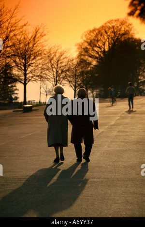 Ältere Paare ohne Gehhilfen machen an einem späten Herbstabend einen Spaziergang entlang der Promenade in Shaftesbury Dorset in Richtung Sonnenuntergang Stockfoto