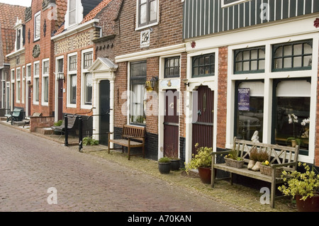 Reihe von kleinen typischen niederländischen Backsteinhäusern in Edam Nordholland mit Bänken und Topfpflanzen entlang einer kopfsteingepflasterten Straße. Stockfoto