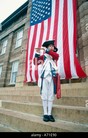 Mann in Coloniel Kleidung vor eine große Flagge der Vereinigten Staaten spielen eine Pfeife am 4. Juli Stockfoto