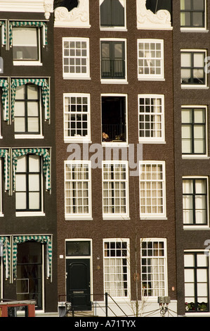 Traditionelle Fensterreihe in einem Mietshaus in Amsterdam, Niederlande. Klassische niederländische Architektur mit Ziegelfassaden und dekorativen Markisen. Stockfoto