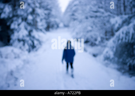 Einsame Frau zu Fuß auf dem Schnee bedeckt Straße umgeben von Bäumen in einem Wald Inverness Schottland Stockfoto