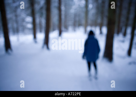 Einsame Frau zu Fuß auf dem Schnee bedeckt Straße umgeben von Bäumen in einem Wald Inverness Schottland Stockfoto